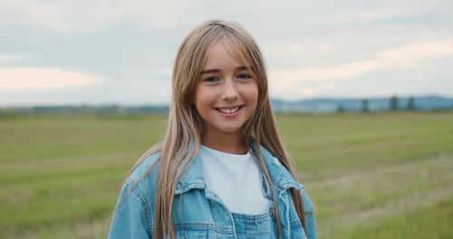 Portrait of Attractive Blond Small Girl Standing in the Green Field with Beautiful Sunset.