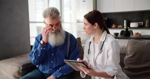 Doctor Reviews Tablet with Senior Man on Couch