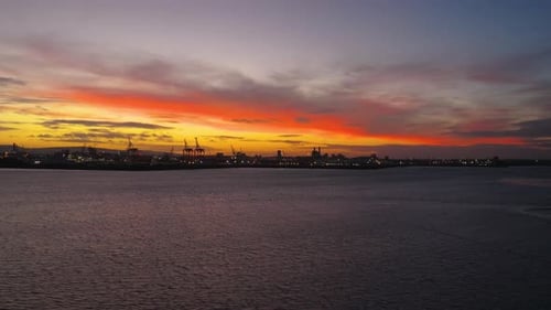 Dramatic Orange Sunset Over Water with Distant Cranes