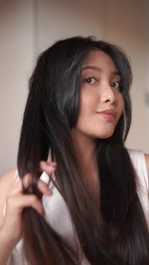 Woman Applying Product to Long Straight Hair Indoors