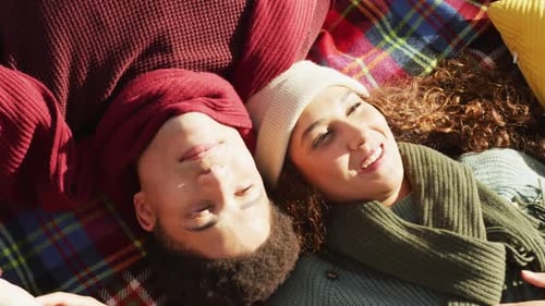 Video of biracial couple warmly dressed lying on blanket spending time in the garden