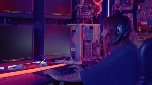 Woman Hacker Sitting in Front of a Computer Typing on Keyboard Hacking Servers in Neon Light Female