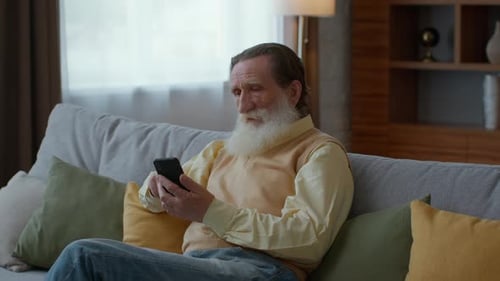 Senior Man Using Smartphone Relaxing on Sofa at Home
