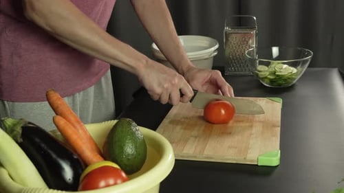 Hands of middle man european slices a tomato with kitchen knife on cutting board, left side view
