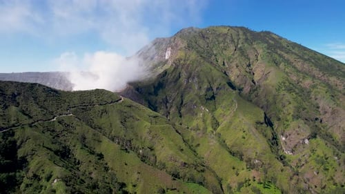 Nahaufnahme des Randes eines dampfenden Vulkans Ijen mit einem türkisfarbenen See und nebligen, bewölkten Bergen