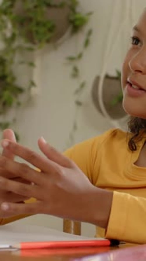 Vertical video: Leaning child in yellow gesturing at table with paper donning headset listening