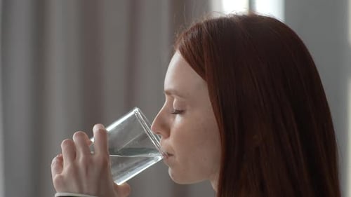 Nahaufnahme des Gesichts einer durstigen jungen rothaarigen Frau mit Glas, trinken Sie Getränke, stilles Wasser, genießen Sie natürliches
