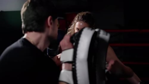 Woman in Gym Preparing to Punch with Boxing Gloves Focused and Intense Training with a Male Trainer