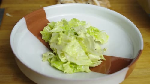 Caesar-Salatmischung in einen tiefen Teller auf einem Holzschneidebrett in der Küche geben. Nahaufnahme in Zeitlupe.