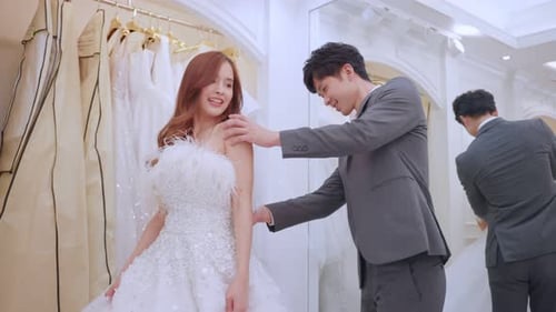 Asian beautiful bride trying on wedding gown with her fiance in studio.