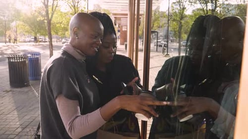 Two women looking in store window holding coffees