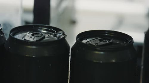 Black aluminum cans rotating on conveyor belt in beverage factory