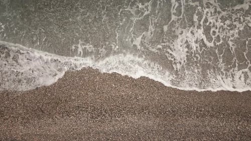 Capturing overhead waves washing onto pebble beach shoreline in afternoon