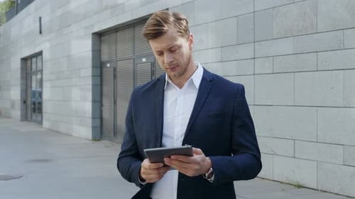 Stressed businessman working on digital tablet waiting for partner in urban city street