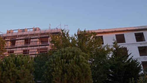 Sitio de construcción con dos edificios de apartamentos adyacentes detrás de árboles verdes