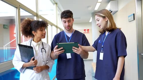 Medical Team Discussing Patient Information on Tablet in Hospital Corridor