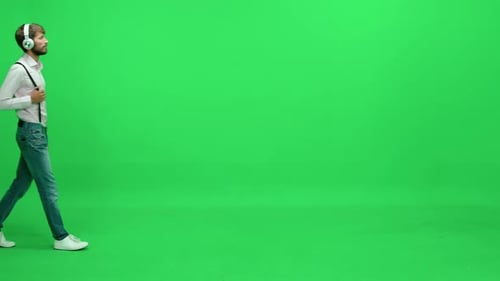 Passerby Man in a White Shirt Walks on a Green Background Listening to Music with Headphones