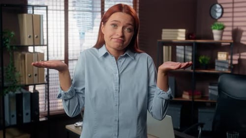 Uncertain Young Red-Haired Woman Shrugging Shoulders in Modern Office