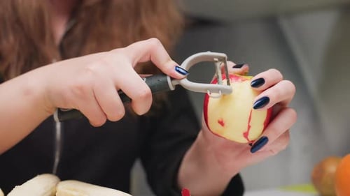 Woman Peels an Apple with Peeler in Kitchen