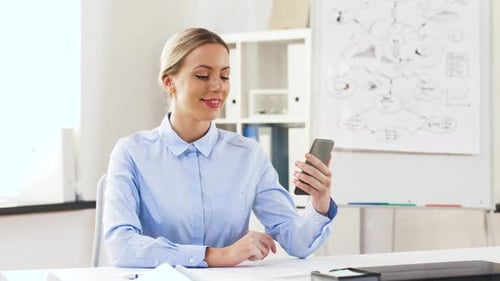 Happy businesswoman waving hand during video call on smartphone in modern office