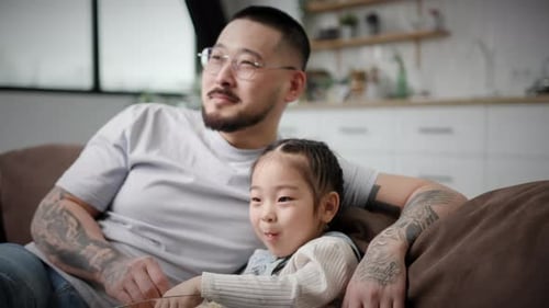 Father and Daughter Relaxing on Couch with Popcorn