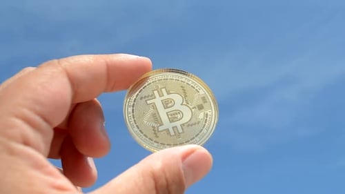 Hand Holding Bitcoin Against Blue Sky