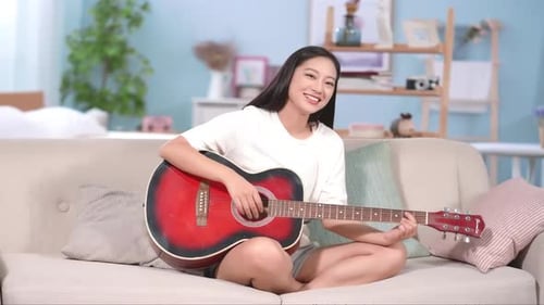 Woman plays the acoustic guitar on the couch