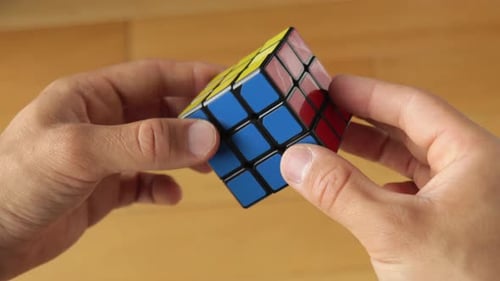 mãos brincando com o cubo de rubik resolvido sem marca, de cima para baixo, ainda veja de perto o interior médio