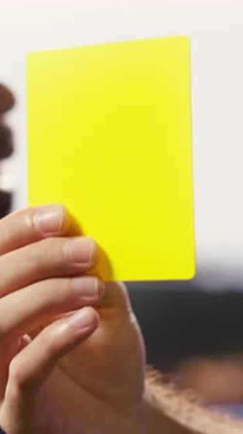 Vertikale Videonahaufnahme einer gelben Karte, die von der Hand des Schiedsrichters nach einem Regelverstoß während des Spiels gehalten wurde