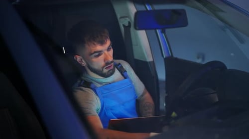 Automechaniker mit Laptop sitzt auf dem Fahrersitz und überprüft Softwarefehler im Fahrzeug