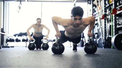 Young Fit Couple in Gym Doing Push Ups on Kettlebells Abdominal