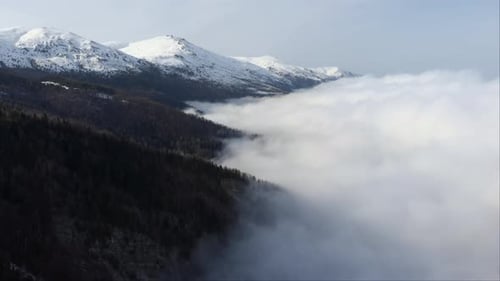 Aerial view of beautiful Mountainside covered in floating clouds snow covered mountain peak at the d