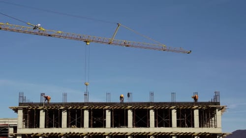 Tower crane bringing materials to workers on last flat of building installing & fabricating ground b