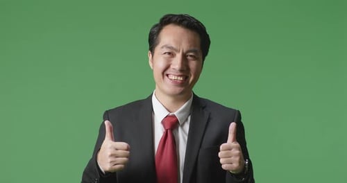 Asian Business Man Showing Thumbs Up Gesture And Smiling While Standing In The Green Screen Studio