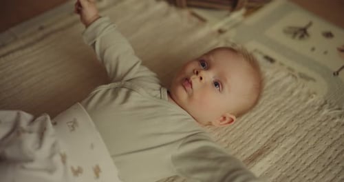 Cute baby lying on blanket indoors, raising arm