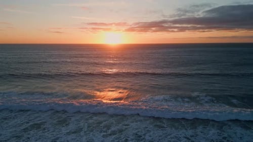 Golden dawn sky reflects on serene ocean surf at sunset slow motion aerial view