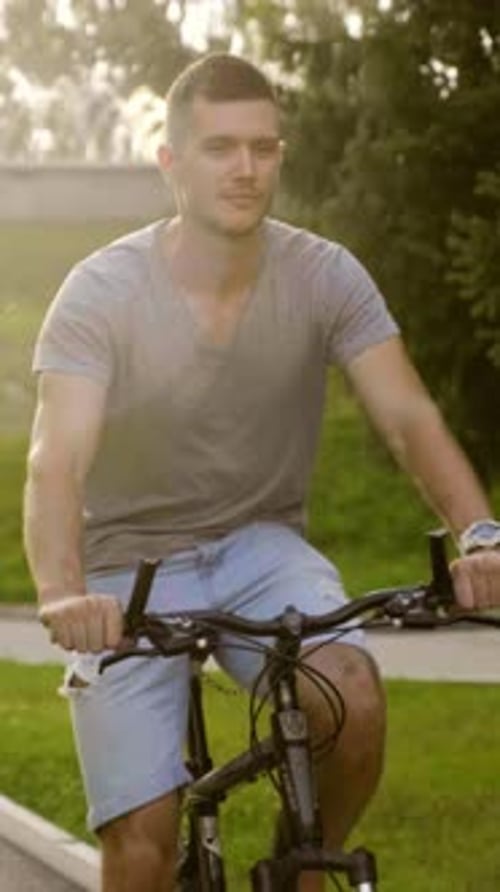 Young Man Riding Bicycle Outdoors in a Park Surrounded By Lush Greenery and Sunlight
