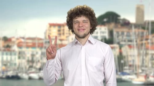 Portrait of a Handsome Smiling Man with Curly Hair Gives Victory Gesture Sign