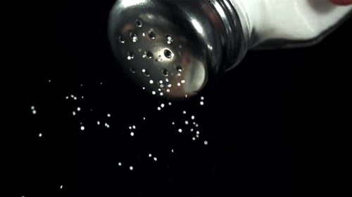 La sal cae de un salero sobre un fondo negro filmada con una cámara de alta velocidad a 1000 fps