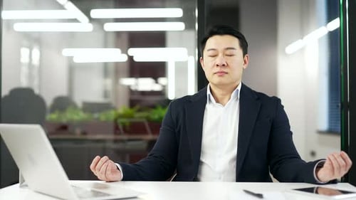 Asian businessman is meditating while sitting at workplace in business office. Entrepreneur