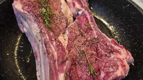 Big red beef stake on a black pan with rosemary ready for cooking, black pepper on top