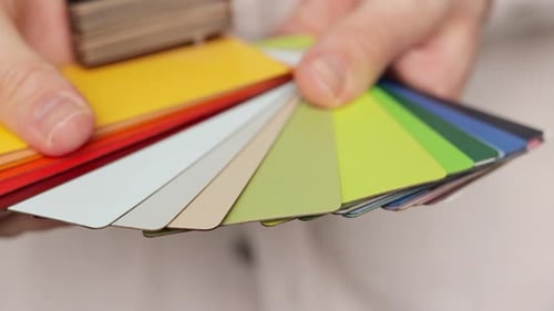 Close up on hands of man designer holding color palette at home. Male person choosing material for r