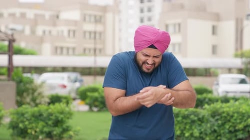 Man in Turban Experiencing Wrist Pain Outdoors