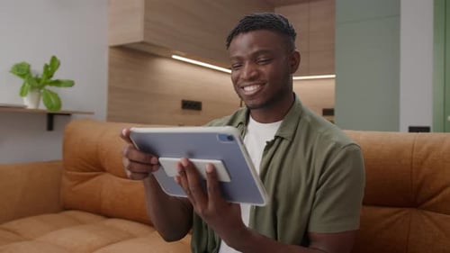 African American Man Browsing Tablet Computer on Couch Black Male Working Online Using Digital