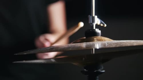 Drummer Hitting Cymbal with Drumsticks in Dark Studio