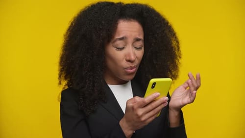 Woman Frustrated Using Smartphone on Yellow Background