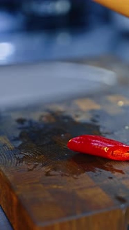 Chef cutting red hot chili pepper with a big knife. Cook preparing a dish. Close up. Vertical video.