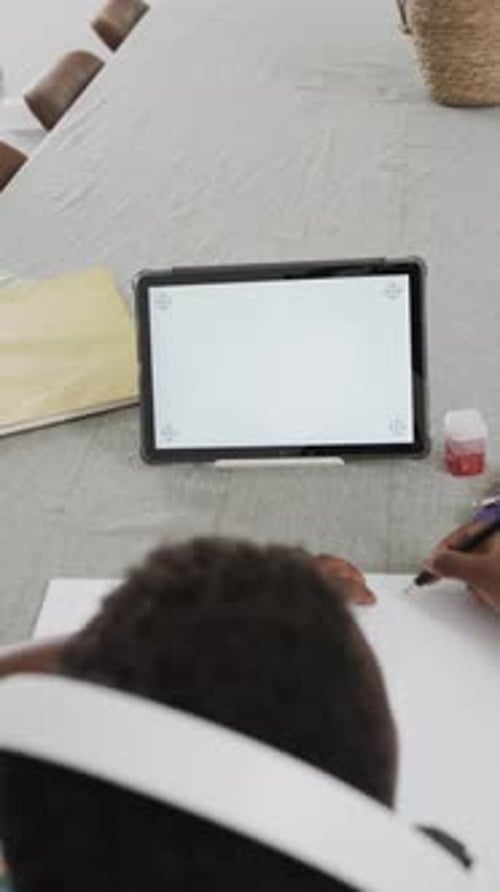 Vertical video: In school, child writing in notebook while using tablet for homework