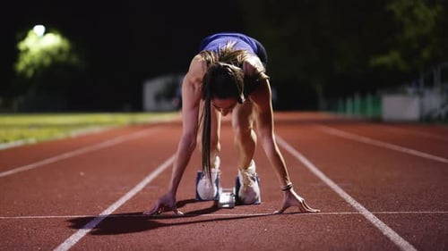 Strong Young Man Starting a Race From Track Starting Blocks Position on a Dark Stadium in the