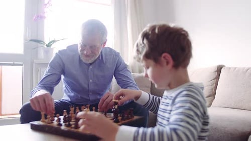 Älterer Großvater mit einem Enkel, der zu Hause Schach spielt